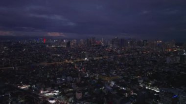 İleri, akşam şehrinin üzerinde uçar. Yoğun şehir gelişimi ve işlek cadde. Arka planda modern yüksek binalar var. Manila, Filipinler.