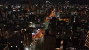 Modern şehirdeki yerleşim yerlerinin üzerinden uç. Uzun apartmanların ve aydınlık sokakların gece hava görüntüleri. Osaka, Japonya.