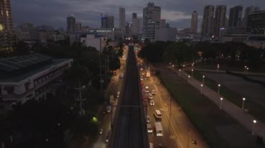 Akşamları işlek caddelerin üzerinde ilerliyorlar. Çok şeritli yolun ortasındaki yüksek demiryolu hattı. Manila, Filipinler.