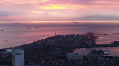 Deniz kıyısının romantik günbatımı görüntüsü. Kargo limanının havadan görünüşü, kıyı boyunca giden gemiler ve renkli gökyüzü. Manila, Filipinler.