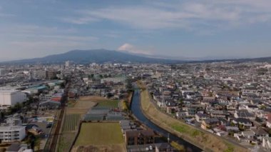 Öğleden sonra güneşli şehir manzarası. Nehir boyunca yerleşim yerlerindeki binalar ve Fuji Dağı 'ndaki ikonik kar örtüsü. Japonya.