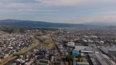 Şehrin havadan panoramik manzarası. Şehir banliyölerindeki dar nehir boyunca alçak binalar altın saatinde güneş ışığıyla aydınlatılıyor. Japonya.