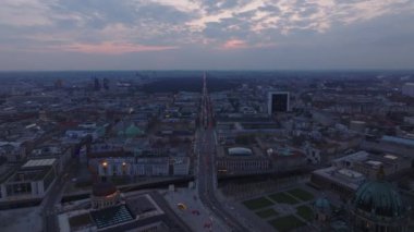 Alacakaranlıkta Berlins canlı şehir manzarası Unter Den Linden, Brandenburg kapısı ve Tiergarten kırmızı bulutlu gökyüzü altında.