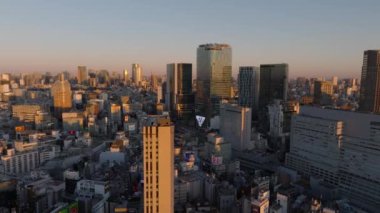 Gün batımında Metropolis 'teki şehir merkezinin üzerinde ilerliyorlar. Gökyüzüne karşı parlak cepheli yüksek binalar. Tokyo, Japonya, 10 Şubat 2024