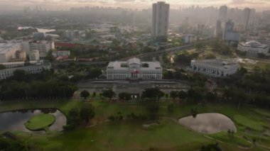 Manila 'daki Ulusal Güzel Sanatlar Müzesi' nin hava görüntüsünde bir golf sahası, şehir silueti ve bulutlu gökyüzü altında yeşil manzaralar yer almaktadır..