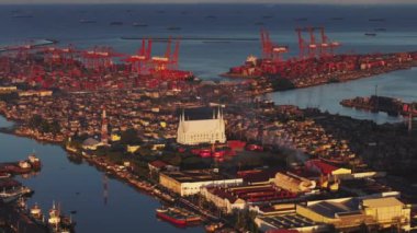 Gün batımında Manila limanının havadan görüntüsü, işlek liman alanı, vinçler ve Iglesia Ni Cristo kilisesi, şehrin dinamik atmosferini gösteriyor..