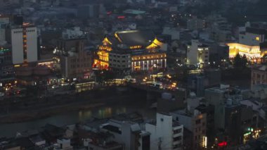 Minamiza Tiyatrosu 'nun aydınlatılmış tarihi binasının ve nehir kıyısındaki işlek yolun hava kaydırak ve pan çekimi. İyi akşamlar şehir manzarası. Kyoto, Japonya, 10 Şubat 2024