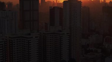 Güneşin çarpıcı görüntüsü bir metropol gökdelenlerinin arkasında batıyor, sıcak renklerle aydınlatılmış şehir silueti üzerinde canlı bir parıltı yayıyor..