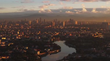 Gün batımında Manila 'nın havadan görünüşü, bulutlu renkli bir gökyüzüne karşı şehrin ufuk çizgisini ve nehri yakalıyor. Kentsel ve seyahat kavramları.