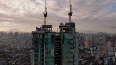Manila 'da inşaat halindeki yüksek bir binanın havadan görünüşü, şehrin arka planında vinçler duruyor..