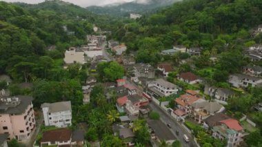 Kandy, Sri Lanka 'da yeşil manzaralar, yerleşim yerleri ve bulutlu bir gökyüzünün altındaki tepelerin yer aldığı bir caddenin hava görüntüsü. Şehir büyüsü yukarıdan.