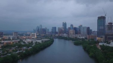 Austins şehrinin ufuk çizgisi ve Colorado Nehri bulutlu bir gökyüzünün altında. Binalar, gökdelenler ve yeşillik manzaralı şehir manzarası.