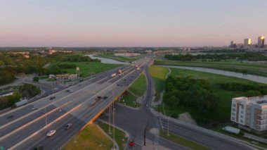 Kamyon ve arabalar gün batımında otoyolda trafiği sağlıyor. Büyük bir Amerikan şehrinde. Arka planda gökdelenler var. .