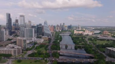 Austin şehir merkezindeki Colorado Nehri 'nin havadan görünüşü modern gökdelenler, yeşil manzaralar ve şehir merkezinde akan su parçalı bulutlu bir gökyüzünün altında sergileniyor..
