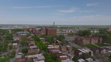 Gökyüzünden St. Louis 'in engin kentsel manzarası, tarihi binalar, sanayi tesisleri, ağaçlı sokaklar ve açık mavi gökyüzünün altında uzak bir ufuk çizgisi sergileniyor..