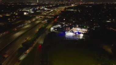 Geceleri Houston çevre yolunun aydınlık binaları ve arka planda şehir silueti olan havadan görüntüsü, kentsel gece hayatı ve ulaşımı yakalıyor..