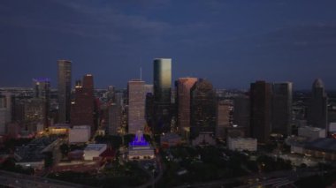 Houston şehir merkezinin hava görüntüsü alacakaranlıkta yükseliyor, akşamdan akşama değişiyor. Canlı ışıklar şehir manzarasını aydınlatır, şehir manzarasındaki yüksek binaları ve gökdelenleri gösterir..