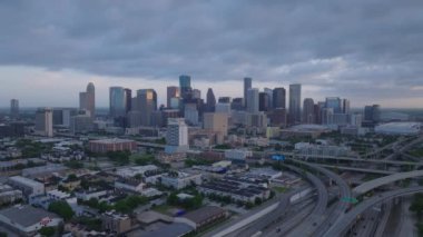 Houstons 'un hava manzarası şafak vakti yükseliyor, dramatik bulutlu bir gökyüzü altında ikonik binalar ve otoyollar var. Kentsel, seyahat ve emlak temaları.