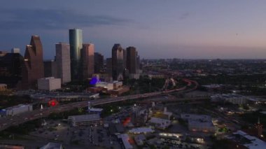 Houston şehir merkezinin alacakaranlıktaki hava manzarası, parlayan gökdelenler ve yoğun otoyollar karanlık bir gökyüzü altında alçalıyor..