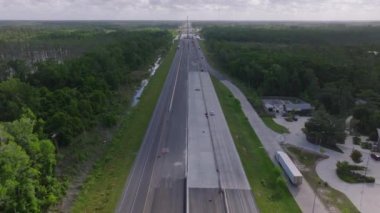Louisiana otoyolunun araçları, yemyeşil ormanları ve bulutlu bir günde park halindeki kamyonları ve binaları olan hava manzarası..