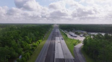 Yeşil bir ormanın içinden geçen Louisiana otoyolunun hava görüntüsü, geçen arabalar ve deniz kenarında bir dinlenme alanı. Seyahat ve ulaşım kavramı.
