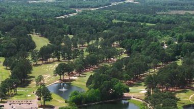 Amerika 'nın güneşli bir gününde yemyeşil ağaçlar ve su kaynaklarıyla çevrili engin bir golf sahasının havadan görünüşü..