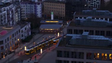 Alacakaranlıkta Berlin 'de işlek bir caddeden geçen tramvayın hava görüntüsü. Yayalar S Bahn istasyonunun yakınına taşınarak Almanya 'daki kentsel yaşamı gözler önüne seriyorlar..