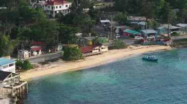 Jamaika 'da bir sahil köyünün sükunetini yukardan yaşayın. Turkuaz sular, renkli evler ve kıyıya demir atmış bir tekne çarpıcı bir kıyı manzarası yaratır..