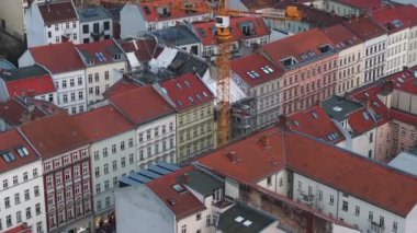 Berlin 'in Prenzlauer Berg bölgesindeki bir yerleşim bölgesinde, kırmızı çatıları ve klasik Alman mimarisi olan binalarla çevrili bir inşaat alanındaki vinç görüntüsü..