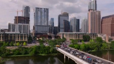 Şehir merkezindeki kalabalık şehir caddeleri ve Colorado Nehri üzerindeki köprüdeki trafik ile Austin 'in gökyüzü manzarası Teksas başkentinin canlı şehir manzarasını gözler önüne seriyor..