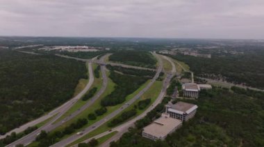 Çevresindeki yemyeşil otobanlar ve bir Amerikan şehrinin kenar mahallelerindeki konut ve ticari binaların hava manzarası..