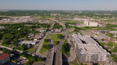 Güneşli bir günde ağaçlar, binalar ve endüstriyel çevresiyle kalabalık bir Amerikan şehrindeki trafiğin hava görüntüsü..