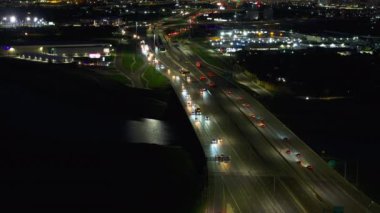 Yoğun bir otoyolun havadan görüntüsü. Büyük bir Amerikan şehrine doğru gidiyor. Canlı ışıkları ve gece ağır trafik akışı var..