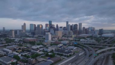 Houstons 'un hava manzarası şafak vakti yükseliyor, dramatik bulutlu bir gökyüzü altında ikonik binalar ve otoyollar var. Kentsel, seyahat ve emlak temaları.