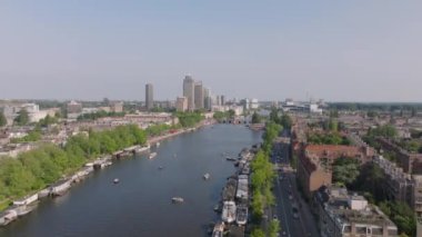 Güneşli bir günde, Amsterdam Kanalı 'nın havadan görünüşü, kıyılar boyunca yüzen tekneler ve binalar, şehirlerin mimarisini ve yeşilliğini aydınlatıyor..