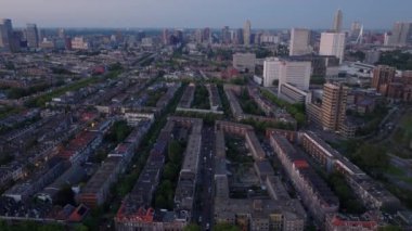 Günbatımında Rotterdam yerleşim bölgesinin hava manzarasında modern gökdelenler ve hareketli alçak evler yer alıyor. Karmaşık sokak şekilleri ve yeşil alanlarla sakin bir akşam ortamı..
