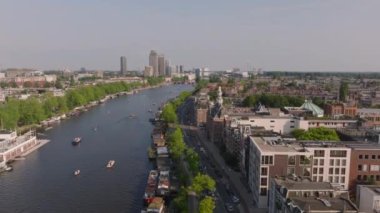 Güneşli bir günde Amsterdam şehir manzarası ve kanalı yüzen evler, geleneksel binalar ve yeşillikler bu canlı Avrupa şehrinin güzelliğini gözler önüne seriyor..