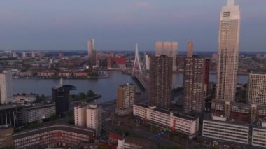 Günbatımında Rotterdam modern mimarisi, ikonik erasmus köprüsü ve De Zalmhaven I iskan kulesi solan ışıkta parlıyor..