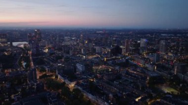Rotterdam kentsel ufuk çizgisi günbatımında, modern binalar, aydınlık sokaklar ve nehir sergileniyor. Şehir manzarası ve mimari görseller.