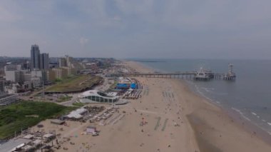 Sahile gidenlerle, renkli çadırlarla ve denize uzanan dönme dolabı olan ikonik rıhtımlı Hagues plajı manzarası..