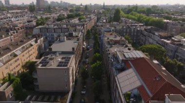 Amsterdam çatıları, ağaç sıralı sokaklar ve güneş ışığıyla yıkanmış şehir manzarası. Kentsel ve mimari temalar.