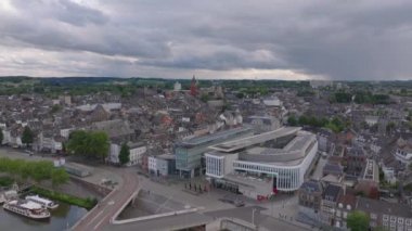 Bulutlu bir gökyüzünün altında sakin bir nehir zeminine karşı modern ve tarihi binaların karışımı ile Maastricht 'in büyüleyici şehir manzarasını keşfedin..