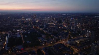 Alacakaranlıkta Rotterdam şehir manzarası. Aydınlatılmış gökdelenleri ve kentsel çevreyi tanımlayan caddeleri olan canlı mimari manzara.