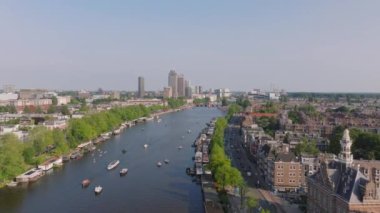 Amsterdam kanallarında tarihi binalar ve yeşilliklerle çevrili teknelerin hava manzarası. Seyahat, mimari ve şehir yaşam temaları.