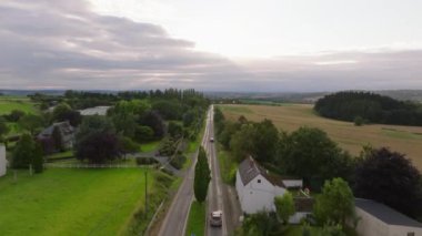 Cilveli kırmızı araba Belçika 'nın büyüleyici kırsal yolu boyunca ilerliyor, bereketli tarlalar ve sık ormanlarla çevrili, kırsal yaşamın sükunetini vurguluyor..
