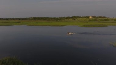 Ringkobing Fjord 'un sakin sularında, sakin kıyı şeridini noktalayan uzak bir evle motorlu bir teknede yüzen bir balıkçıyı görüntüler..