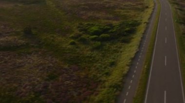 Havadan bakıldığında, Danimarka 'daki Ringkobing Fjord boyunca uzanan sakin bir yol sergilenmekte, bereketli manzaralar ve gün batımında ışıldayan su yansımaları sergilenmektedir..