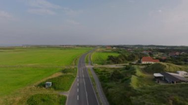 Danimarka kırsalındaki yemyeşil çayırlarda düz bir yolda ilerleyen kamera Kuzey Denizi 'ni ve Ringkobing Fjord' u gösteriyor..
