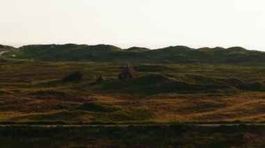 Büyüleyici sazdan çatı kulübeleri berrak gökyüzünün altındaki yemyeşil tepelerin arasında yuva yapar, Danimarka kırsallarında huzurlu bir kırsal güzellik manzarası yaratır..