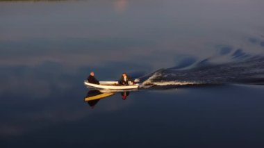 İki balıkçı, Danimarka 'daki Ringkobing Fjord' un pürüzsüz sularında küçük motorlu tekneleriyle sakin bir akşamın tadını çıkarırken, batan güneş sıcacık bir ışıltıyla sahneyi yıkıyor..